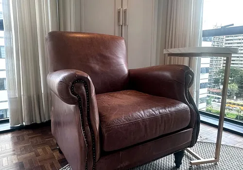 Poltrona de couro para leitura junto à janela do consultório principal, com vista da cidade