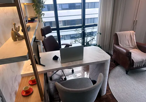 Mesa de atendimento em mármore no consultório principal, com poltrona de couro e luz natural