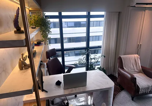 Outro ângulo da mesa de mármore do consultório principal, com notebook e itens de trabalho organizados